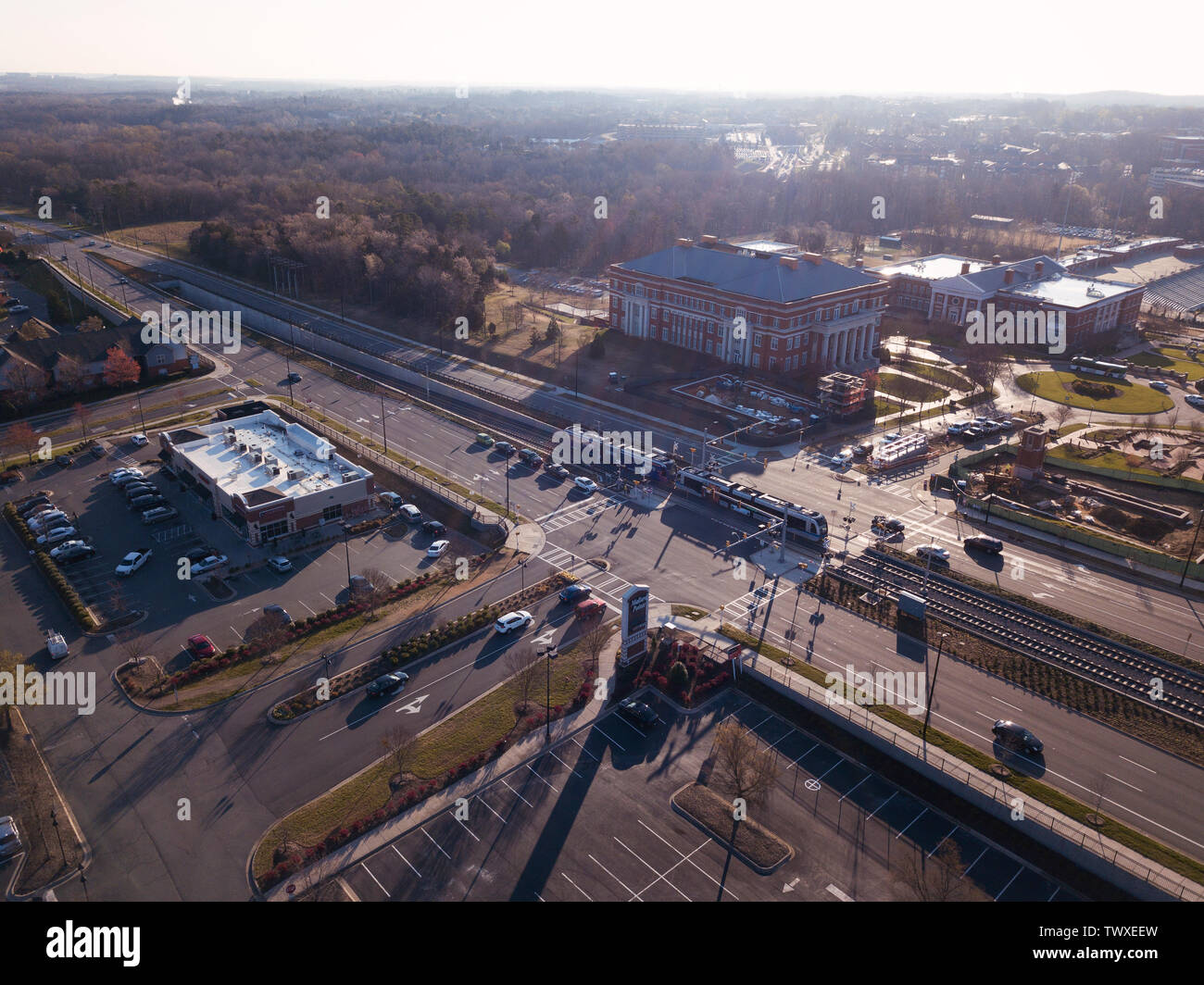 Eine Stadtbahn Zug durch einen Schnittpunkt mit der Universität von North Carolina in Charlotte im Hintergrund an einem sonnigen Morgen Stockfoto