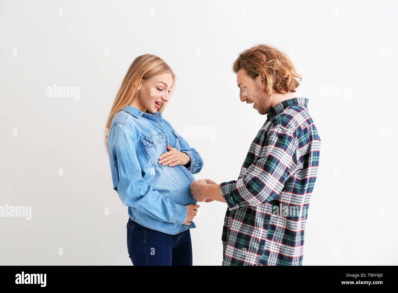 Junge schwangere Frau und ihr Ehemann Vergleich der Größe von ihren Bäuchen auf hellen Hintergrund Stockfoto