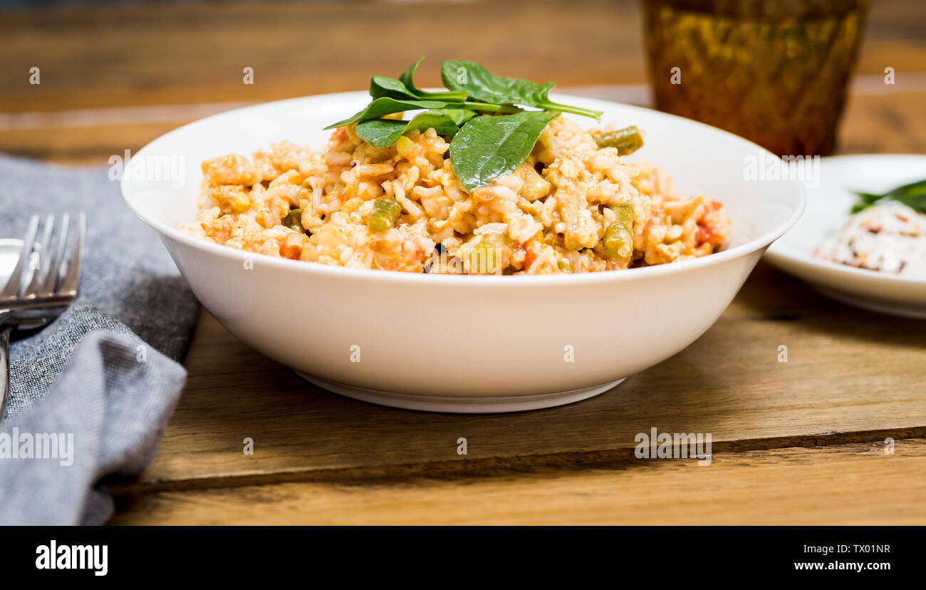 Chicken Curry mit Reis, gekrönt mit Spinatblättern, mit einer Seite der Chili Joghurt, auf einem Holztisch Stockfoto