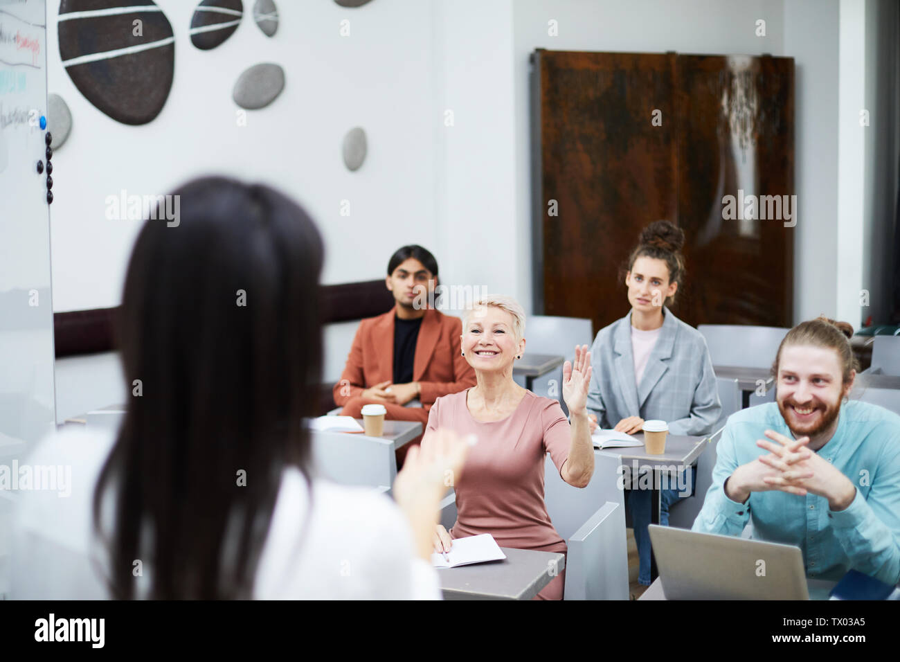 Weitwinkel Portrait von lächelnden reife Frau Hand in der Klasse mit einer Gruppe von Studenten mit Vortrag, Lehrer Sicht Stockfoto