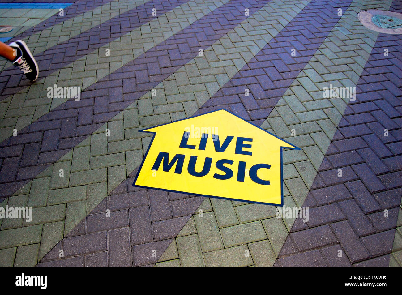 Ein Zeichen in Richtung "Live Musik" auf einem Stein Laufsteg mit einer einzigen Sneaker, die in die entgegengesetzte Richtung gezeigt wird. Stockfoto