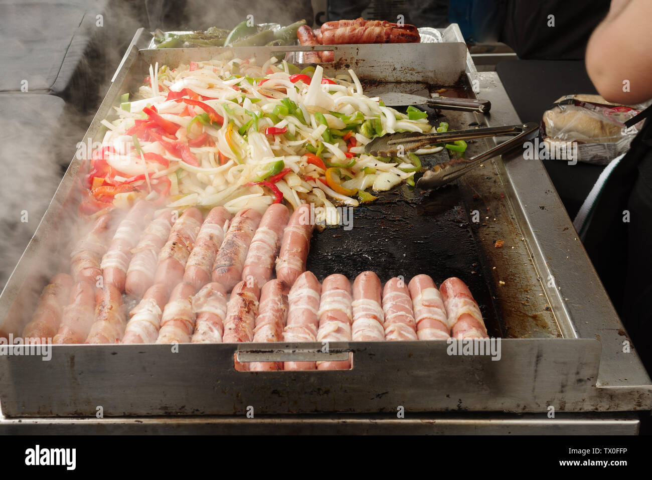 Hot Dogs, Zwiebeln, grüner Pfeffer und rote Paprika kochen auf heißem Grill. Stockfoto