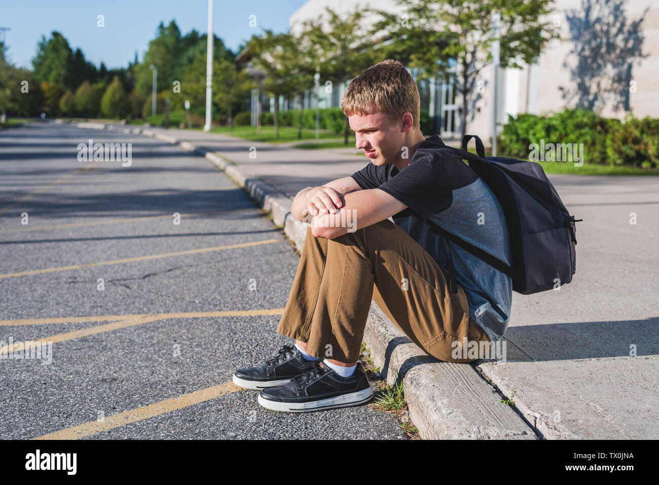 Traurige Teenager Junge sitzt auf dem Bürgersteig vor seiner Schule. Stockfoto