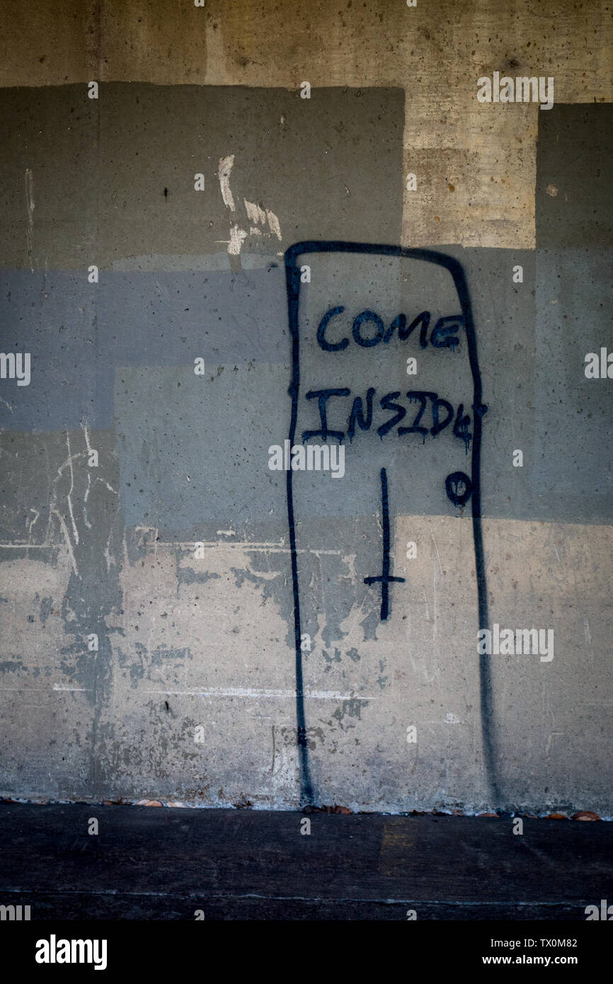 Eine Tür mit einem Kopf Kreuz und die Worte "Komm in' auf eine schmutzige Wand gemalt Stockfoto