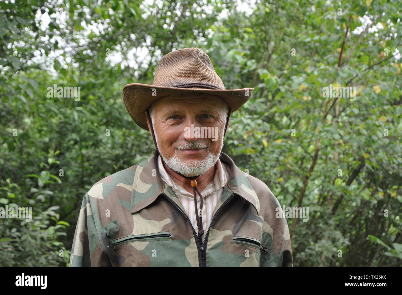 Reisenden mittleren Alters. Porträt einer stattlichen erwachsenen Mann mit grauem Bart und Hut in Camouflage Kleidung vor dem Hintergrund des Waldes Stockfoto