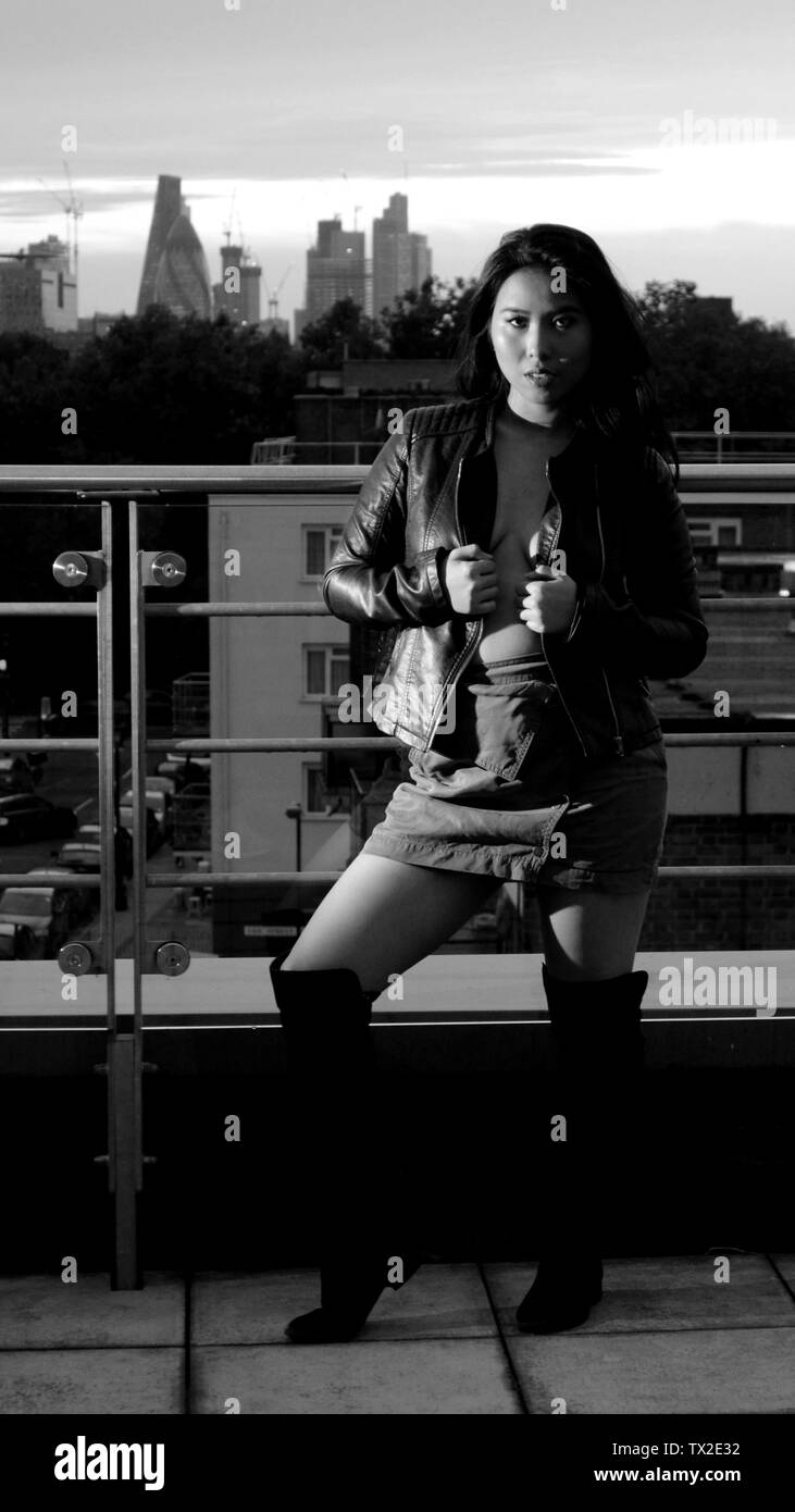 Modell auf einem Balkon, der eine Jacke, Rock und Stiefel, mit Sonnenuntergang über der City von London im Hintergrund. Stockfoto