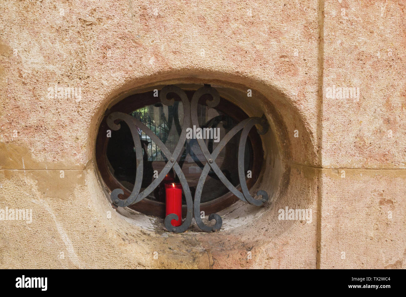 Dekorative latticewor auf dem Oval kleines Fenster. Die rote Kerze auf die Fensterbank. Stockfoto