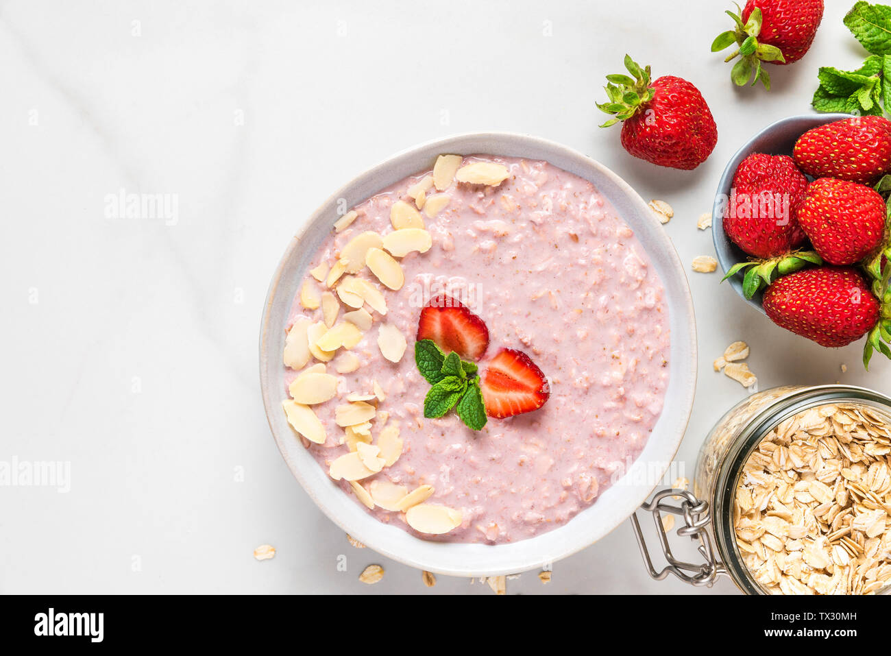 Über Nacht Hafer mit frischen Erdbeeren, Mandeln und Minze in einer Schüssel auf weißem Marmortisch. gesundes Frühstück. top View Stockfoto