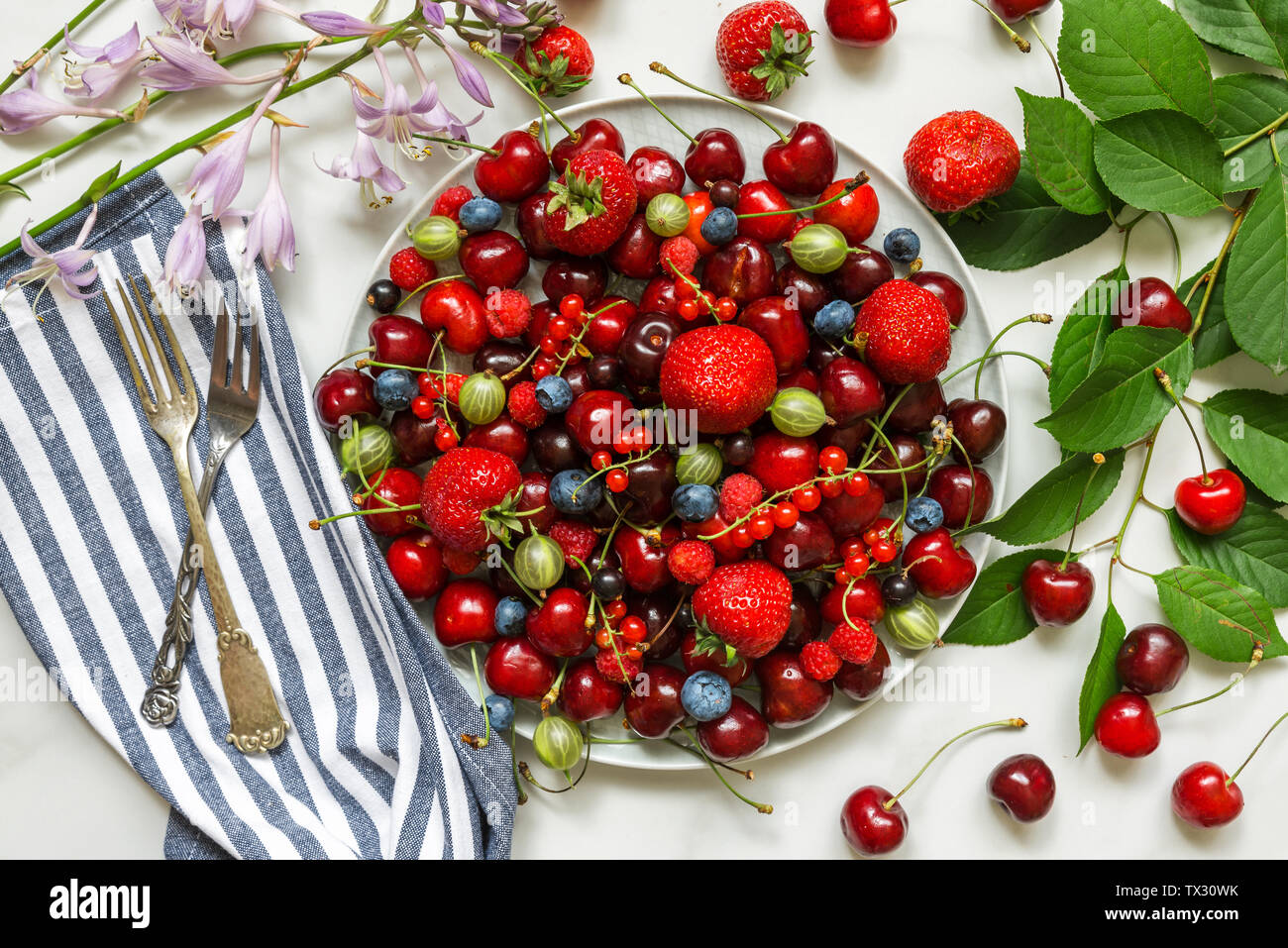 Verschiedene frische Sommer Beeren in einen Teller mit Gabel auf weißem Marmortisch. Ansicht von oben. Gesunde Ernährung Essen. Ernte Konzept Stockfoto