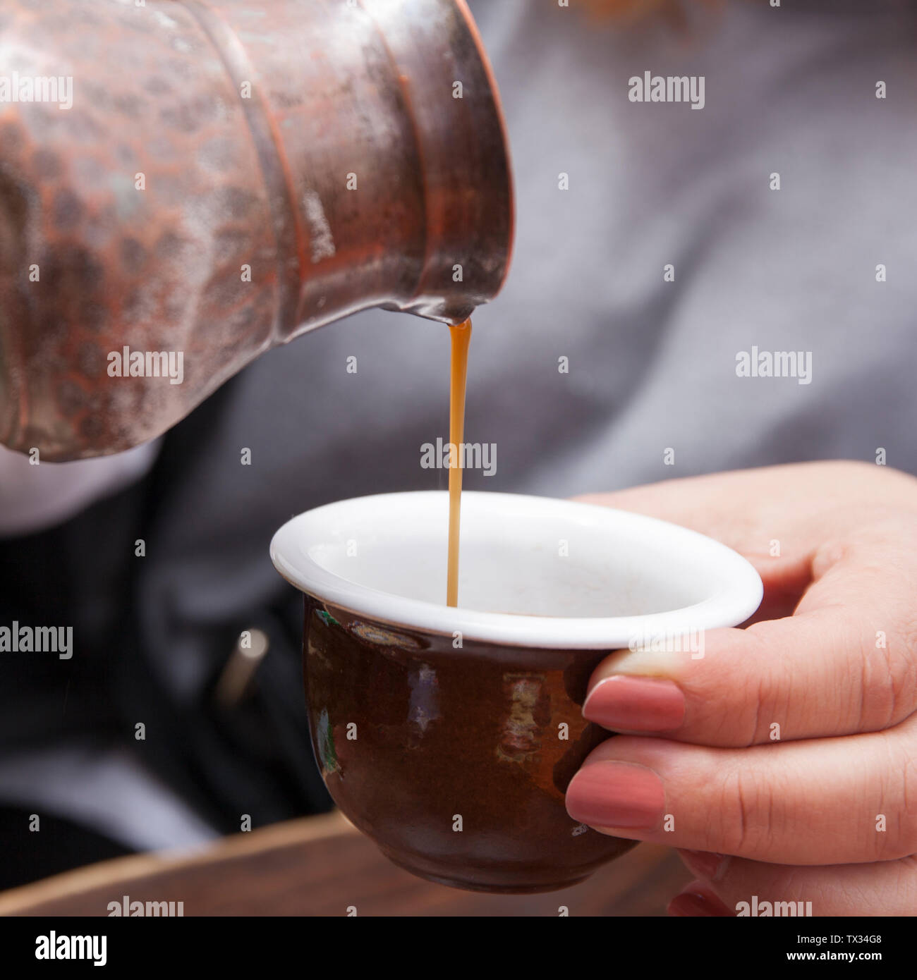 Strömenden heißen Kaffee in einer Keramik Tasse mit einem traditionellen Türkischen Kupfer Kaffeekanne. Stockfoto