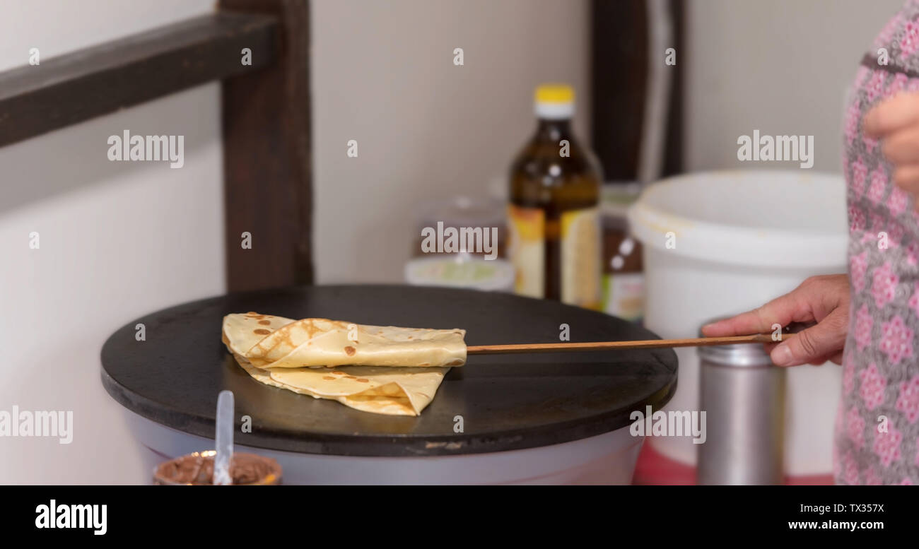 Vorbereitung Crepes auf einer heißen Platte und mit einem langen holzlöffel Falten Stockfoto