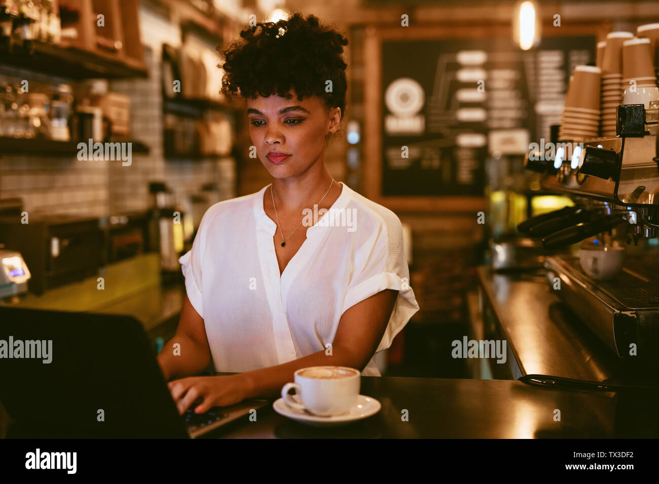 Weibliche cafe Eigentümer an der Theke stehend Arbeiten am Laptop mit einer Tasse Kaffee. Junge Frau mit Laptop an ihrer Coffee Shop. Stockfoto