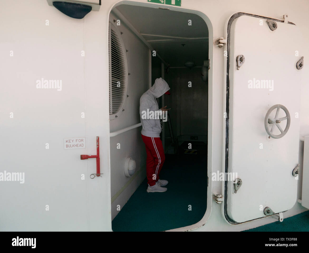 Junger Mann mit smart phone in Tür auf Kreuzfahrtschiff Stockfoto