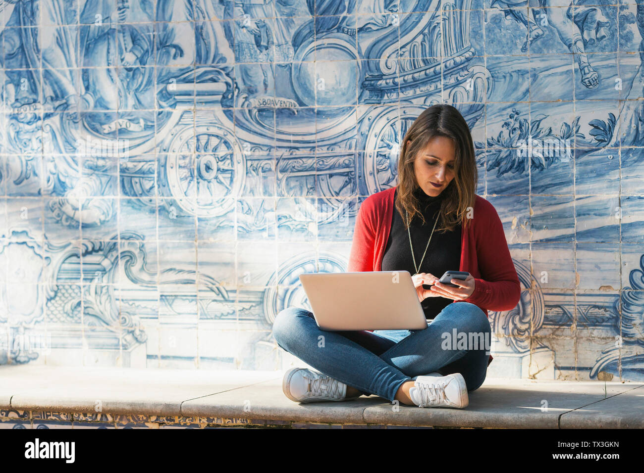 Frau mit Laptop und Smartphone gegen Mosaik Wand Stockfoto