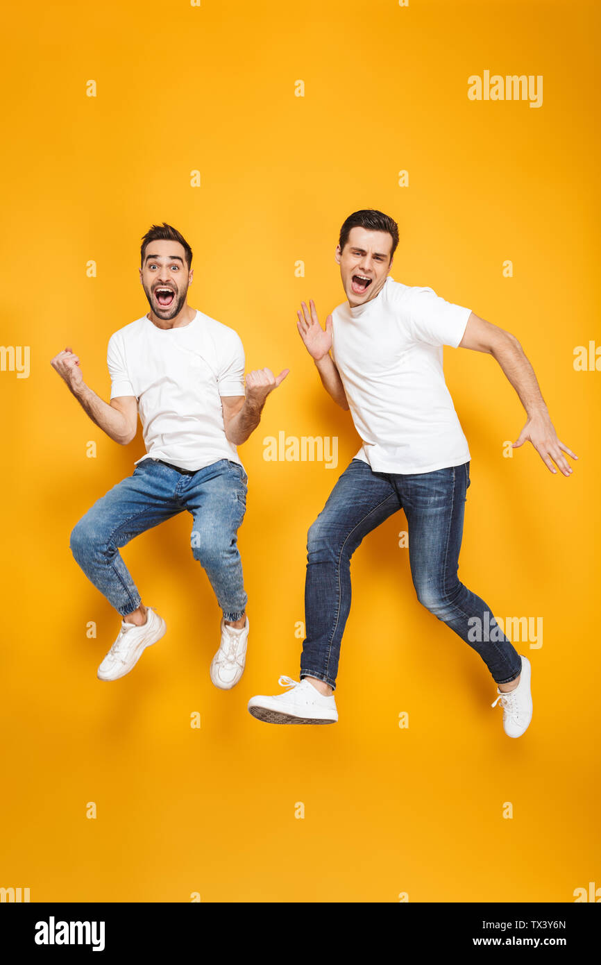 Volle Länge von zwei fröhliche aufgeregt Männer Freunde tragen Leer t-shirts über Gelb Hintergrund isoliert springen, Feiern Stockfoto