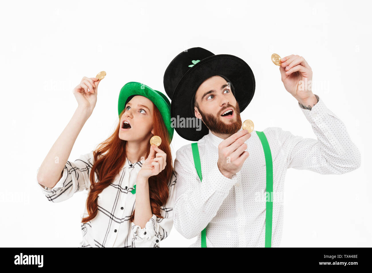 Glückliches junges Paar tragen Kostüme, feiern St. Patrick's Day isoliert auf weißem Hintergrund, goldene Bitcoins Stockfoto