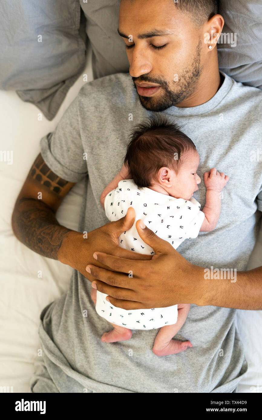 Mann schlafen im Bett sein neugeborenes Baby Holding Stockfoto
