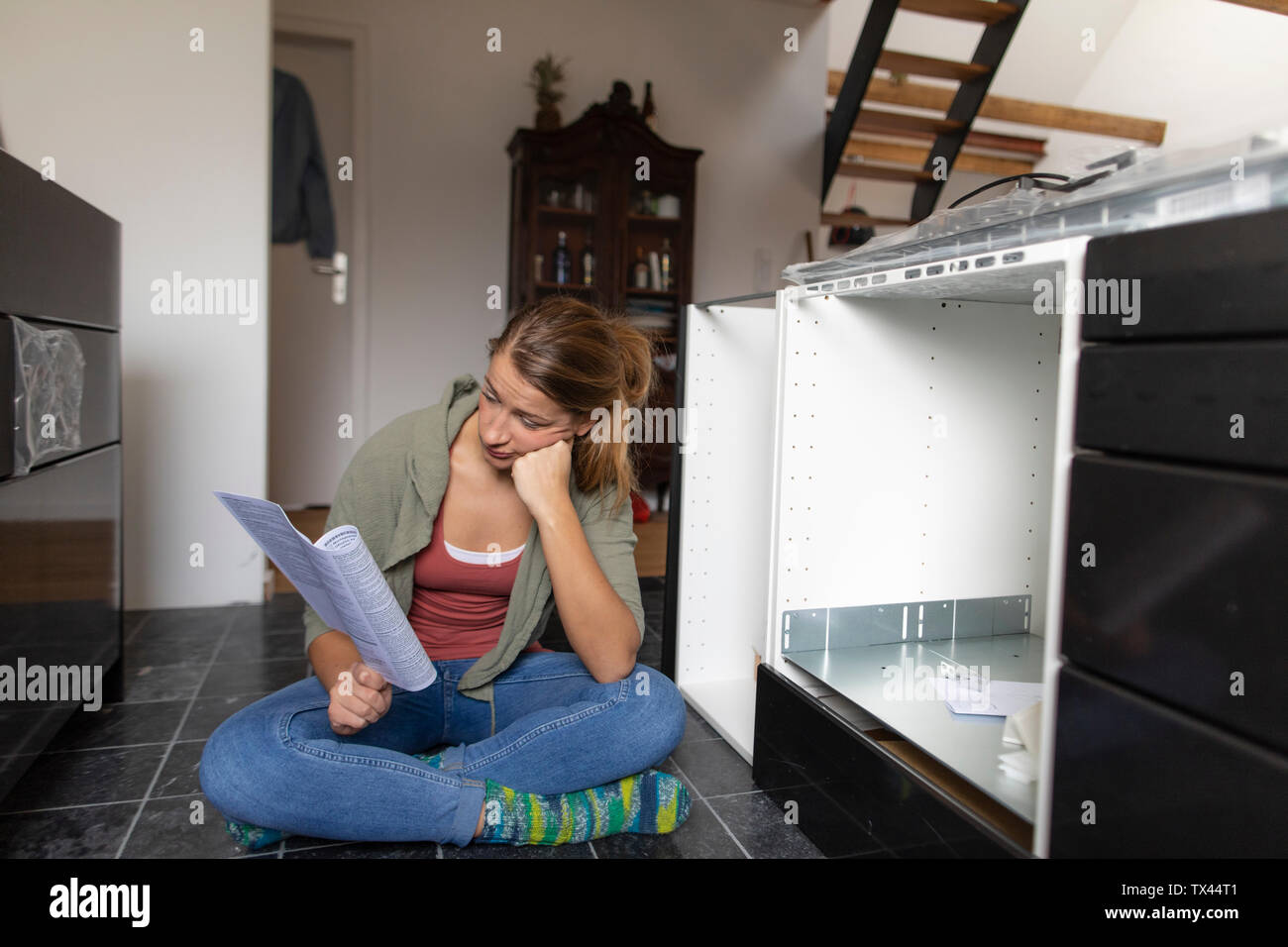 Frustrierte junge Frau liest eine Montageanleitung in der Küche Stockfoto