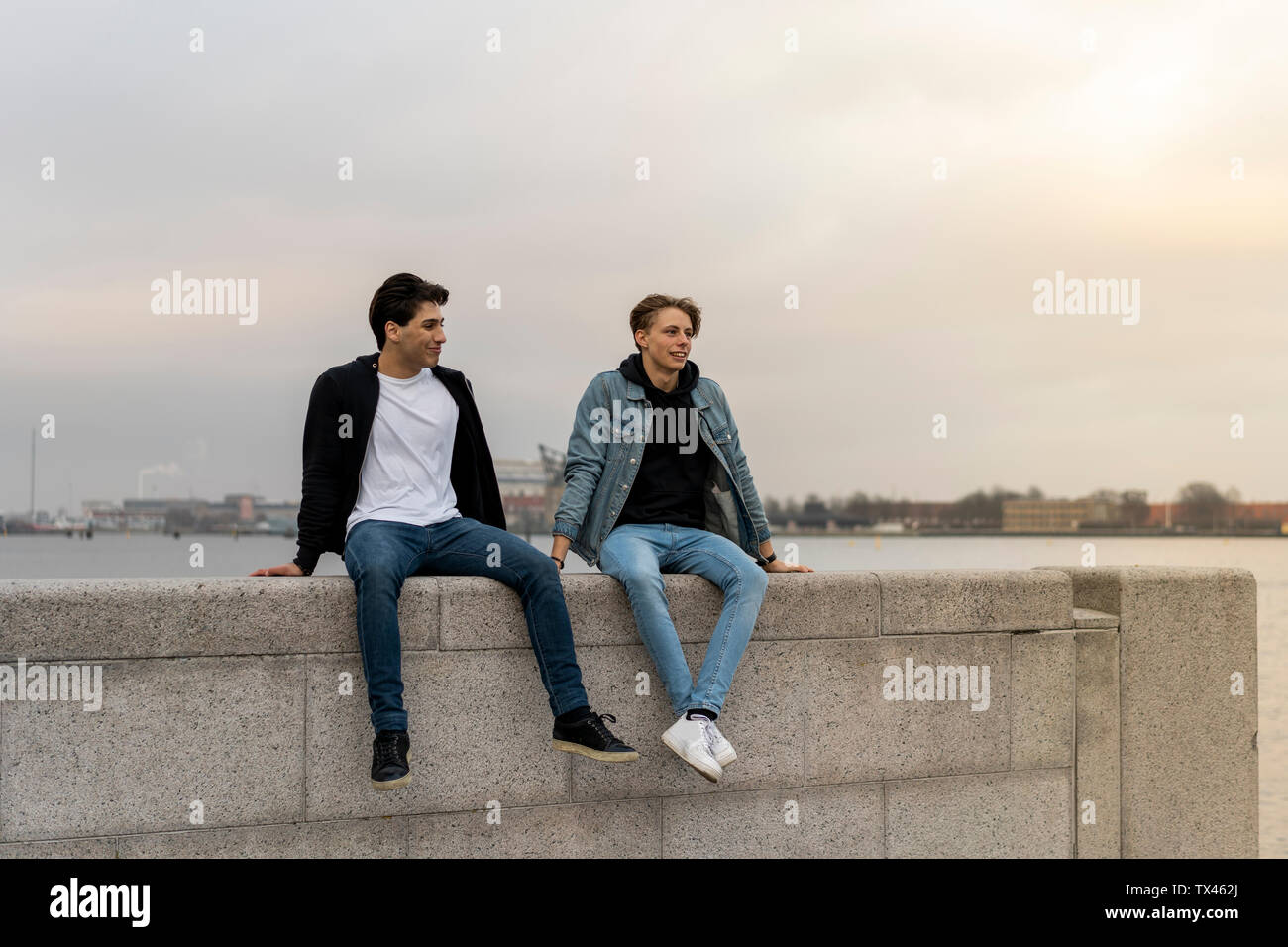 Dänemark, Kopenhagen, zwei junge Männer sitzen auf Wand an der Waterfront Stockfoto