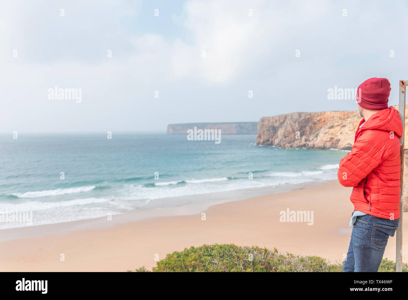 Portugal, Algarve, Lagos, Praia do Beliche, Mann mit roter Mütze und Jacke an den Strand und Meer Stockfoto