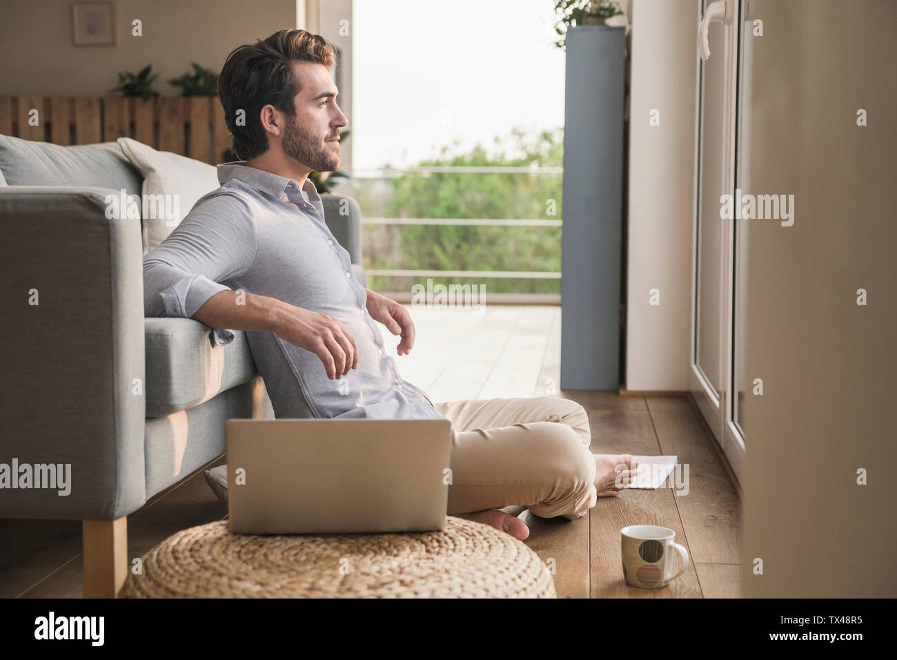 Junger Mann zu Hause sitzen auf dem Boden, mit Laptop, Blick aus Fenster Stockfoto
