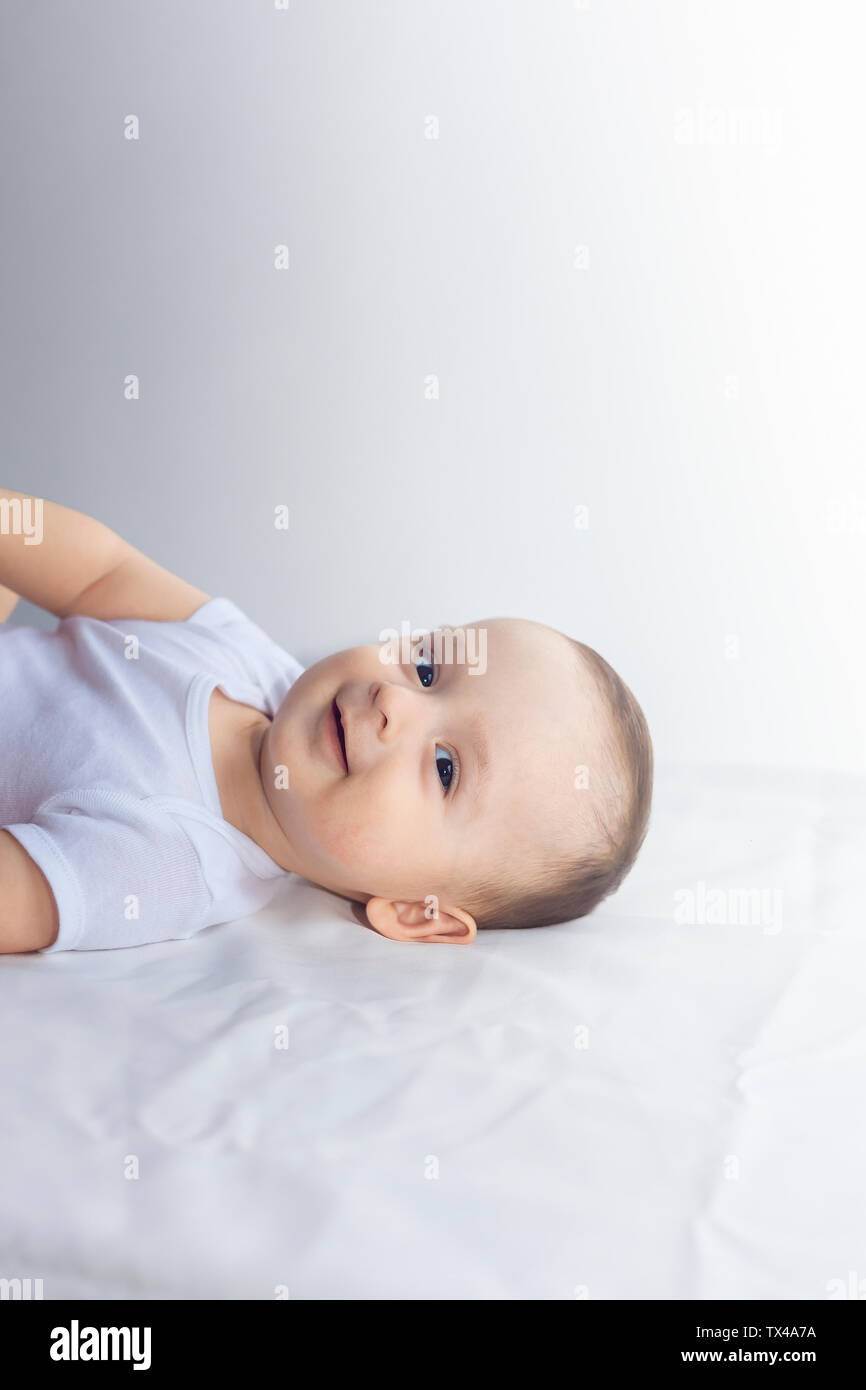 6-monatiges Baby Spaß in weißer Bettwäsche. Cute Baby liegend auf dem Bett. Familie, neue Leben, Kindheit Konzeption. Stockfoto
