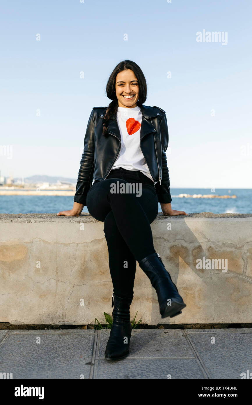Junge Frau sitzt auf einer Wand, Meer im Hintergrund Stockfoto