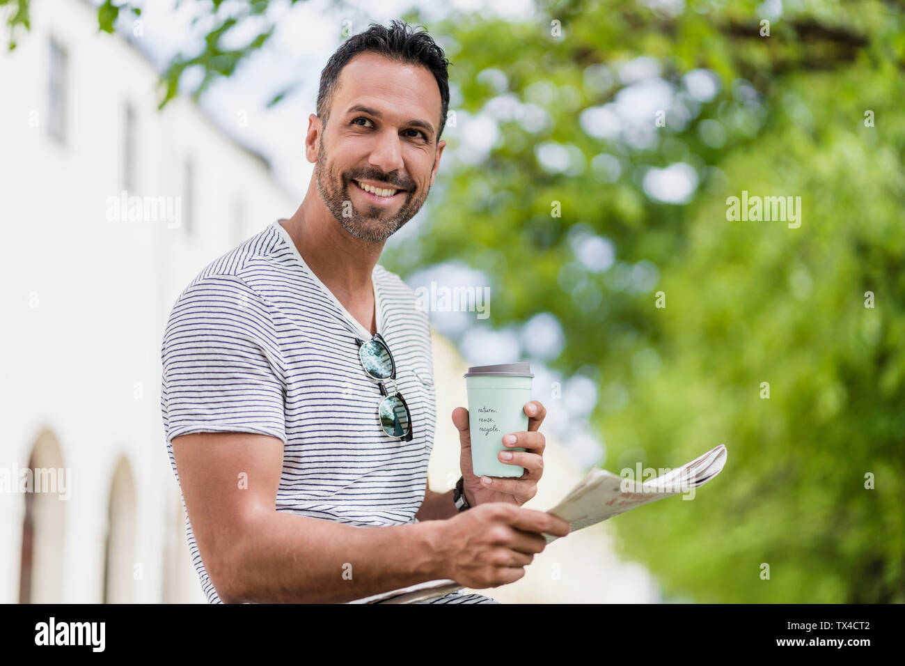 Lächelnder Mann mit Takeaway Kaffee und Zeitung in einem Park Stockfoto