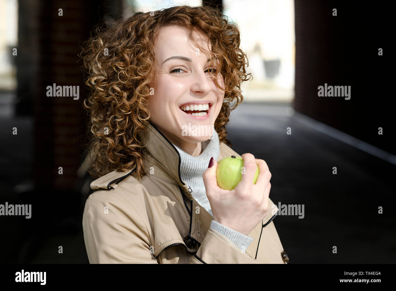 Portrait von lachende Frau mit lockigem Haar mit grünem Apfel Stockfoto