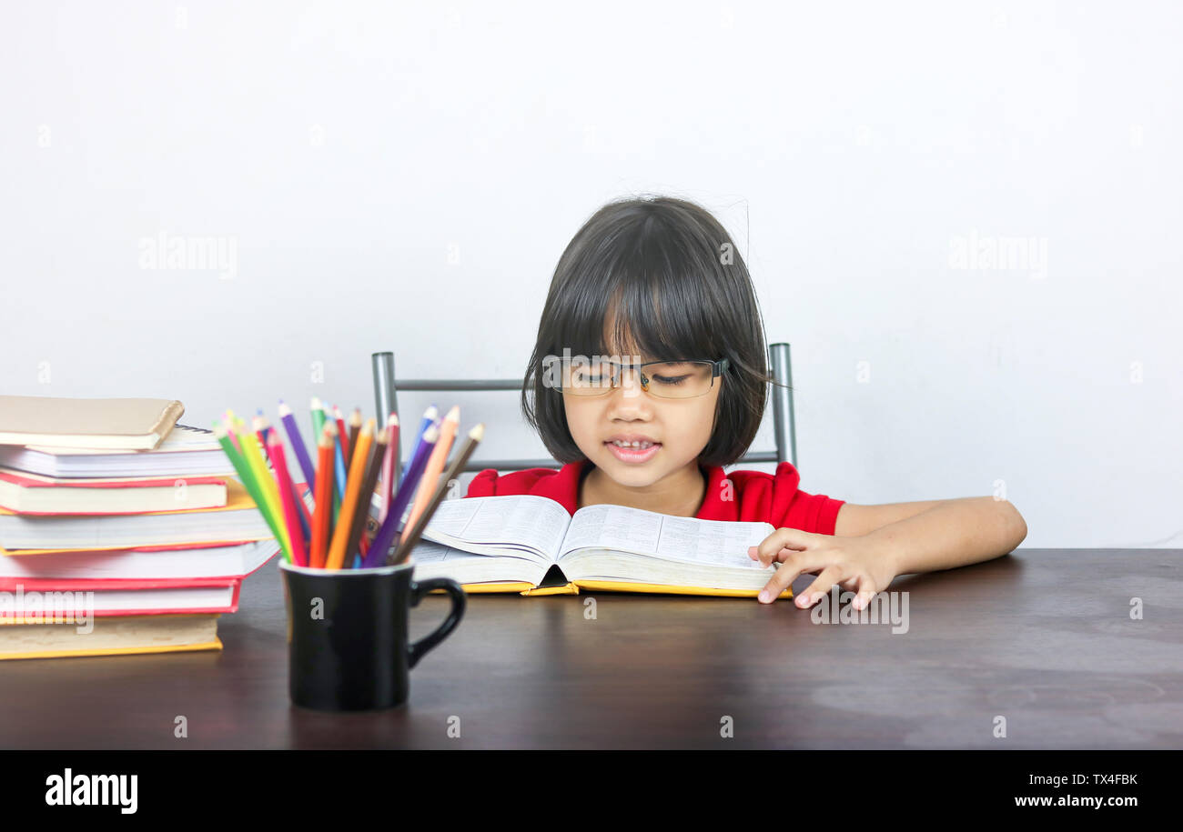 Junge asiatische Mädchen oder Frauen in roten Hemd auf Tisch und lesen Buch sitzen, Konzept, das als Vorbereitung auf die Prüfung und Verbesserung der Intelligenz der Kid Stockfoto