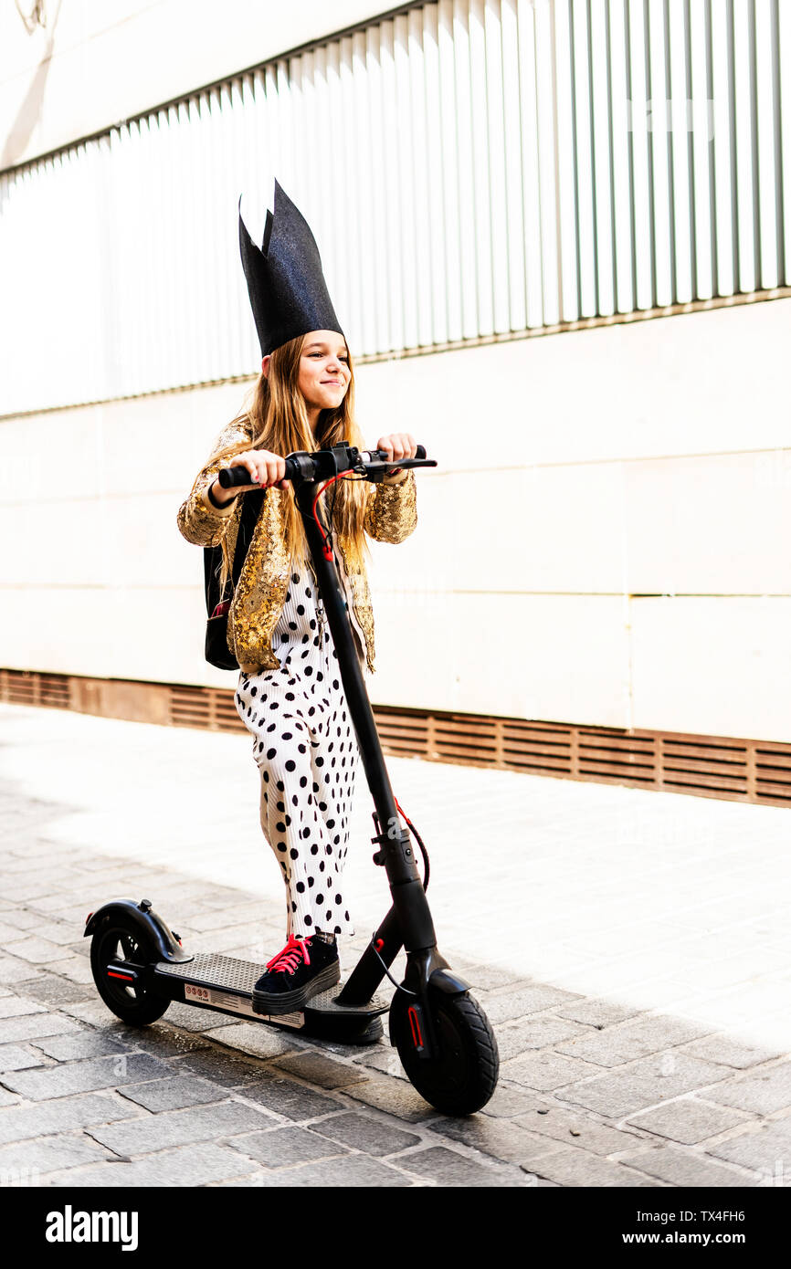 Portrait von lächelnden Mädchen mit E-Scooter mit schwarzen Krone, goldenen Pailletten Jackett und Polka Dot jumpsuit Stockfoto