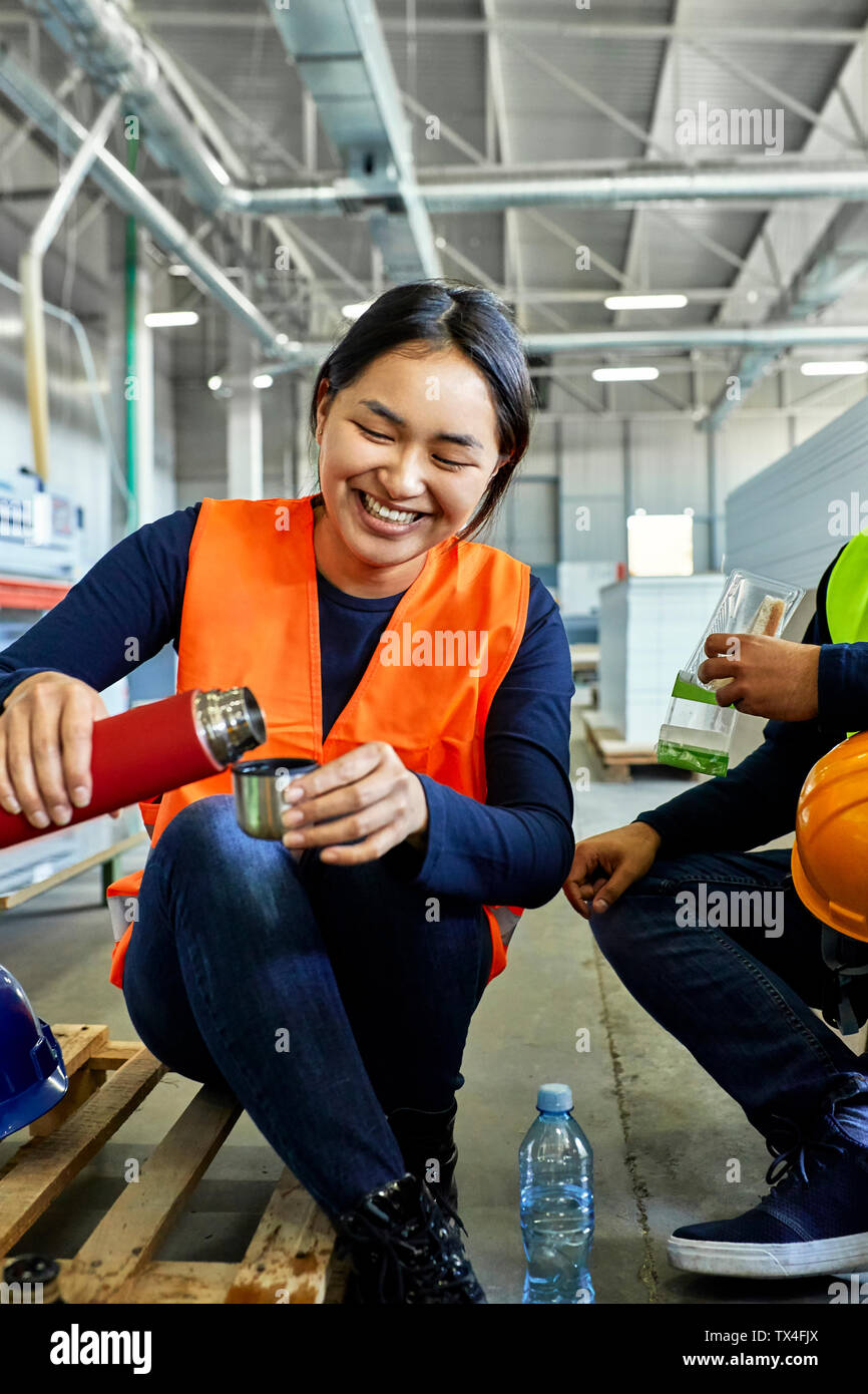 Glückliche Arbeitnehmerin gießen Trinken in Tasse während der Mittagspause in der Factory Stockfoto