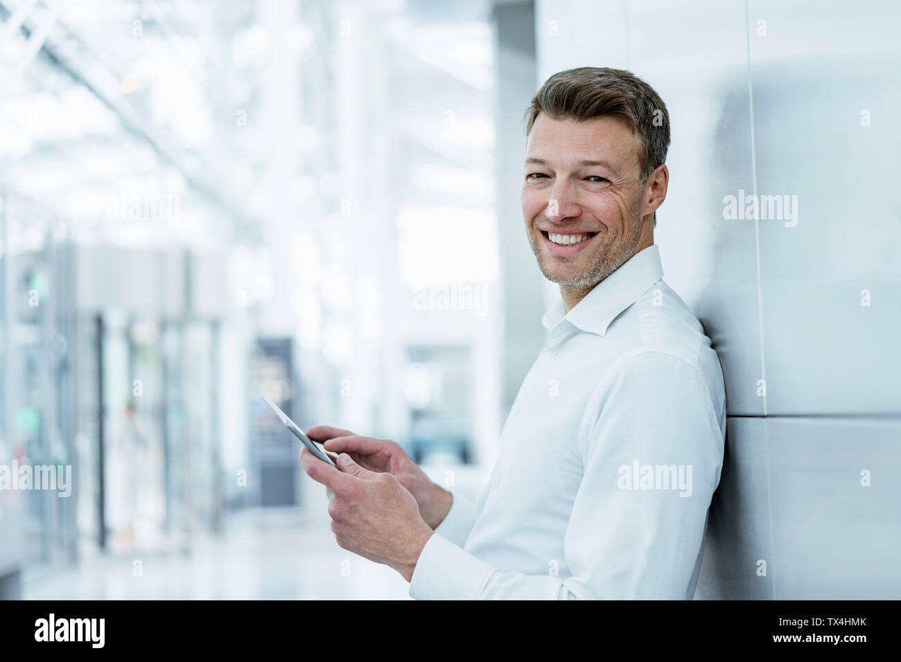 Portrait von lächelnden Geschäftsmann gegen eine Wand holding Handy schiefen Stockfoto