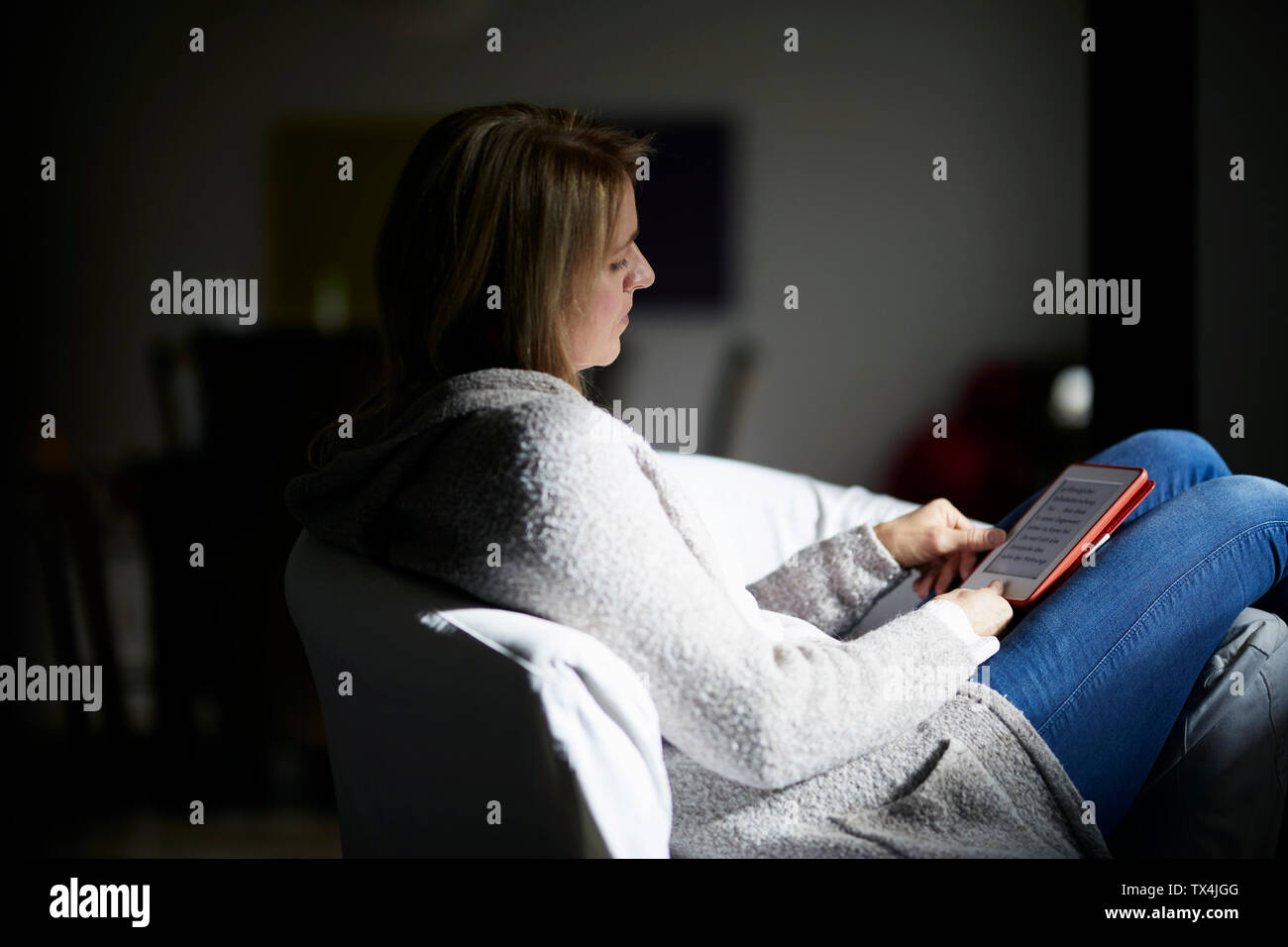 Frau sitzt in einem Sessel, Lesen von E-Books Stockfoto