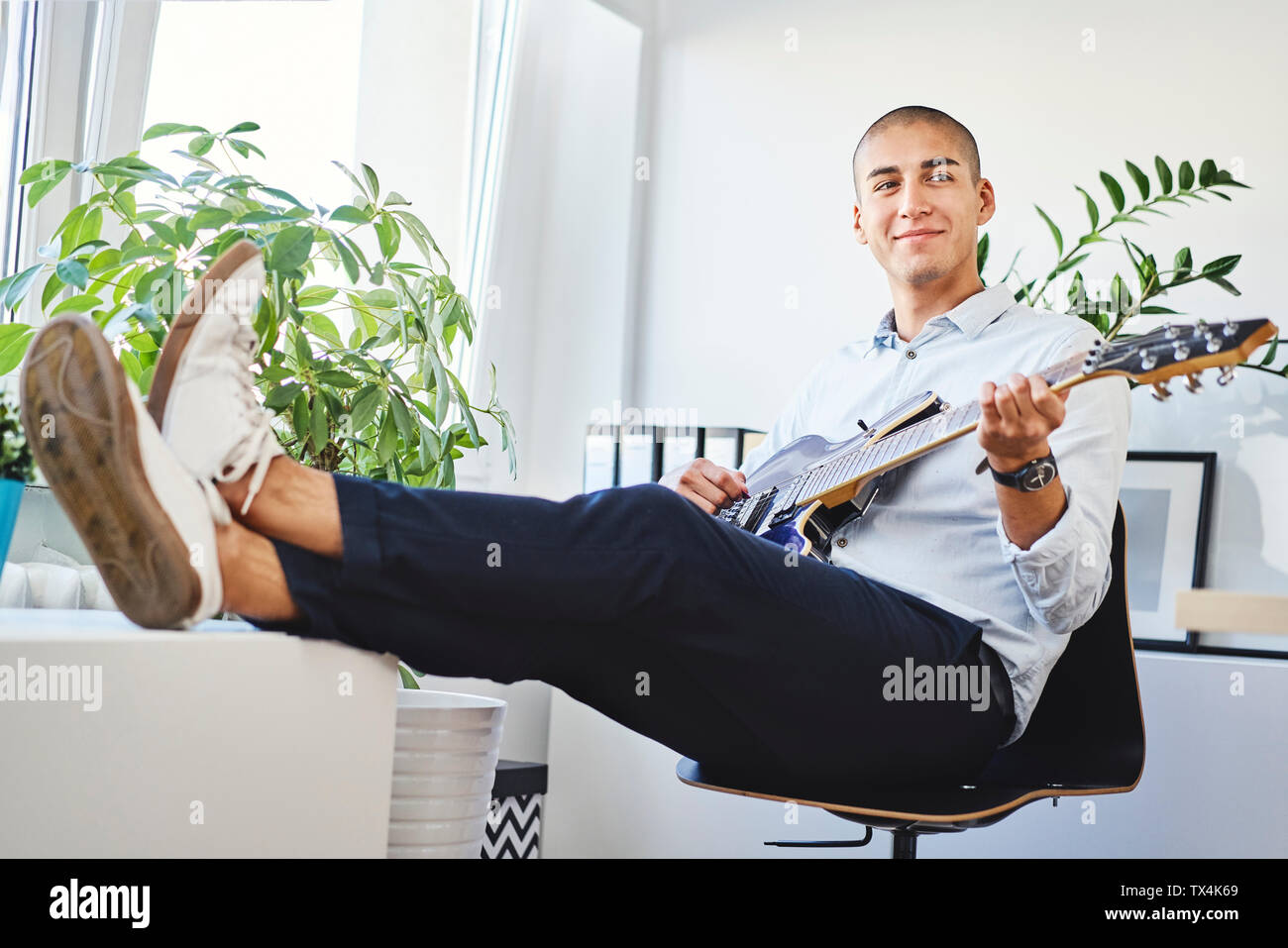 Lächelnden jungen Mann sitzt im Home Office und Gitarre spielen Stockfoto