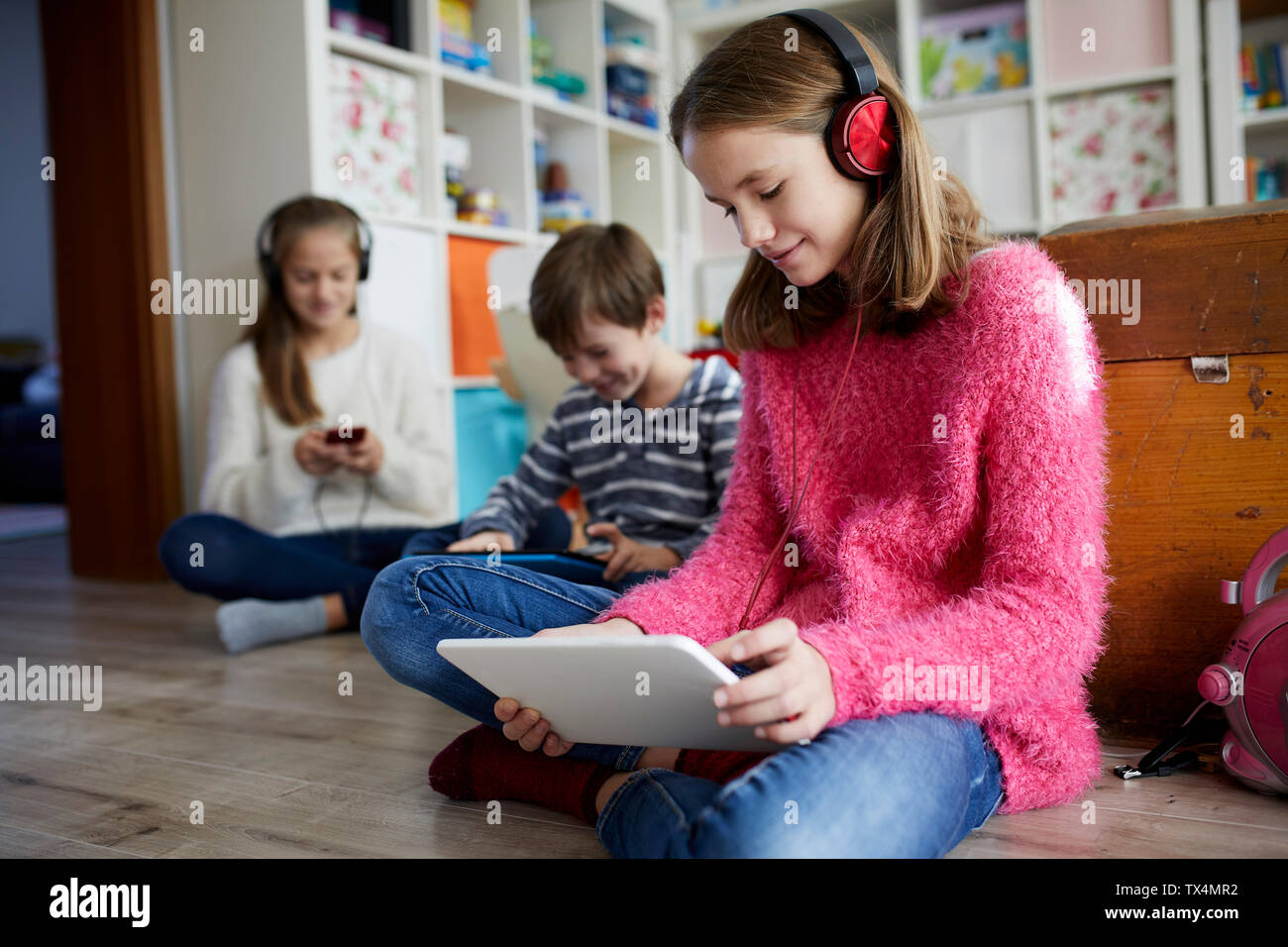 Geschwister spielen zu Hause mit Ihren digitalen Tabletten, sitzend auf dem Boden Stockfoto