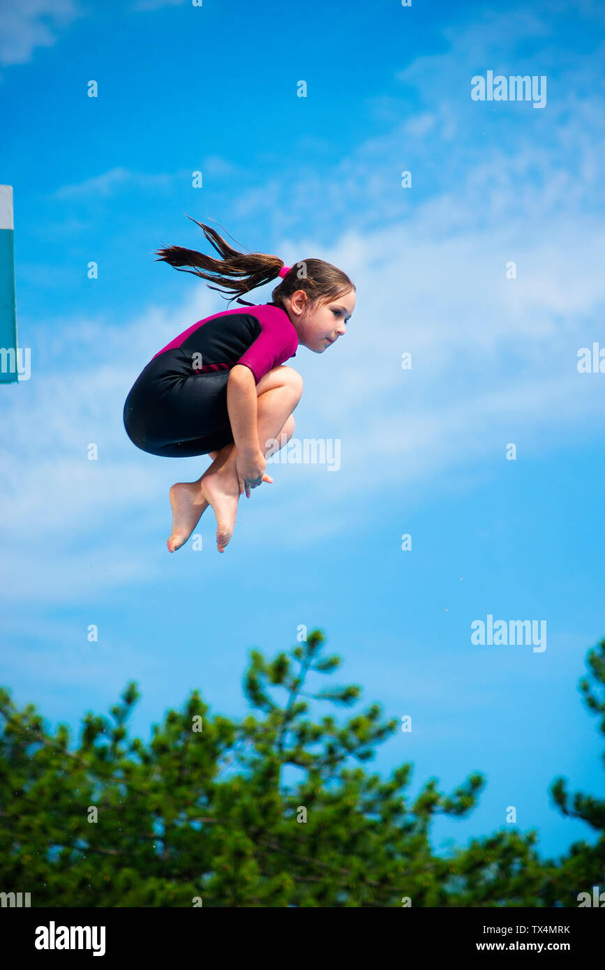 Wenig kaukasisch Weiblich 8 Jahre altes Mädchen in Neopren Shorty surfen  Neoprenanzug springen von 5 mether Sprungturm in crouching Position.  Sommer, s Stockfotografie - Alamy