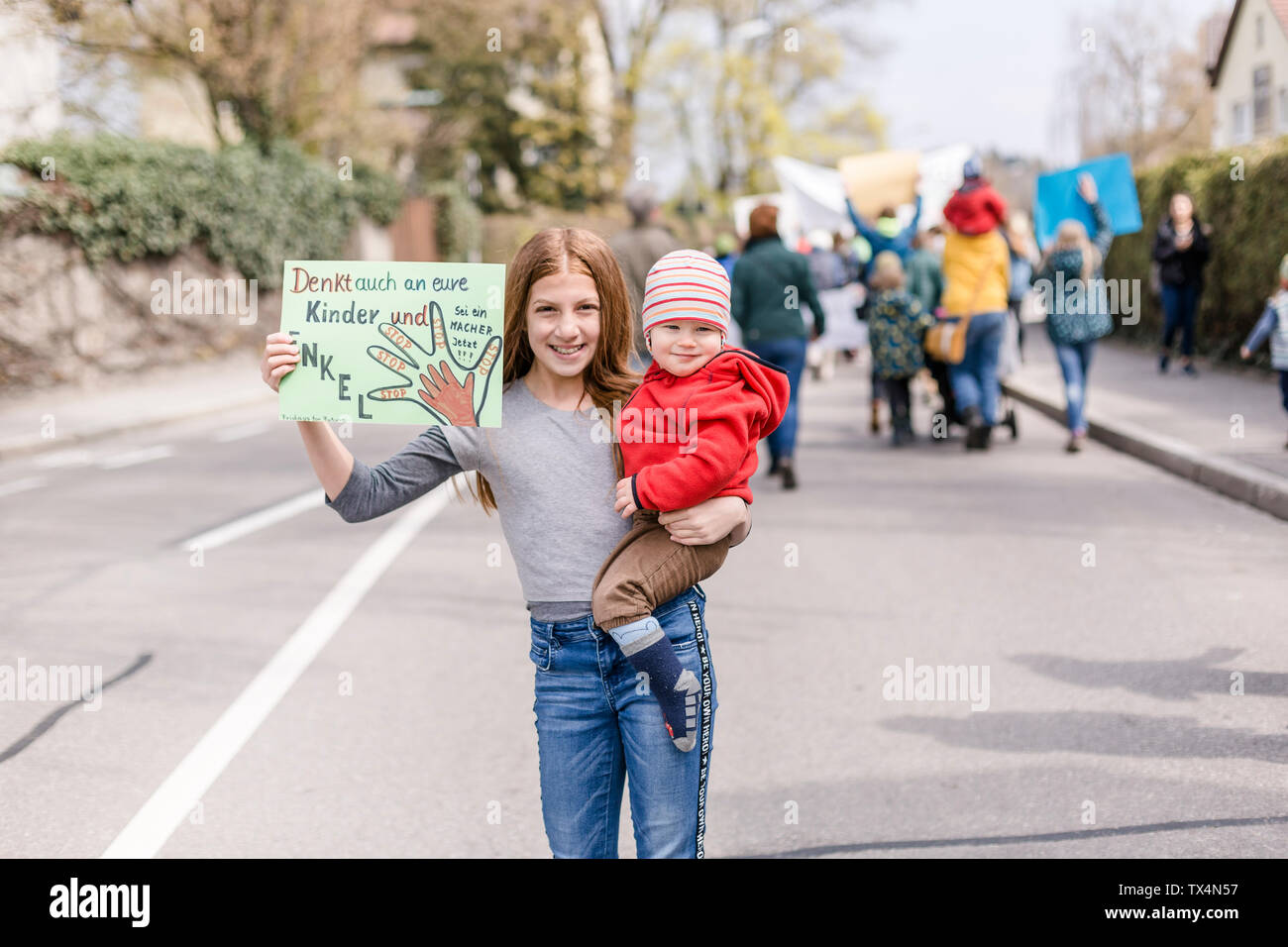 Mädchen mit Baby auf dem Arm hält ein Plakat auf einer Demonstration für den Umweltschutz Stockfoto