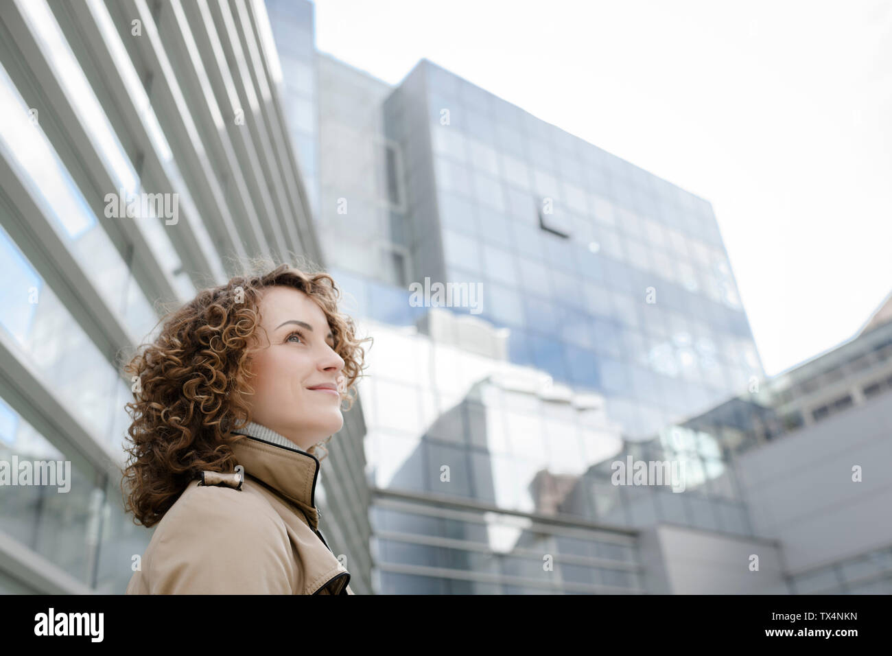 Lächelnde Frau mit lockigem Haar vor der modernen Architektur suchen Stockfoto