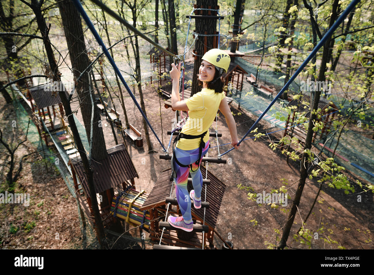 Junge Frau tragen gelbe T-Shirt und Helm in einem Hochseilgarten Stockfoto