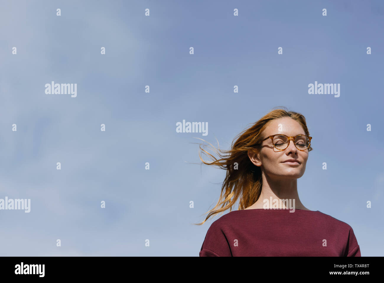 Porträt der jungen Frau mit Brille und geschlossenen Augen unter blauem Himmel Stockfoto