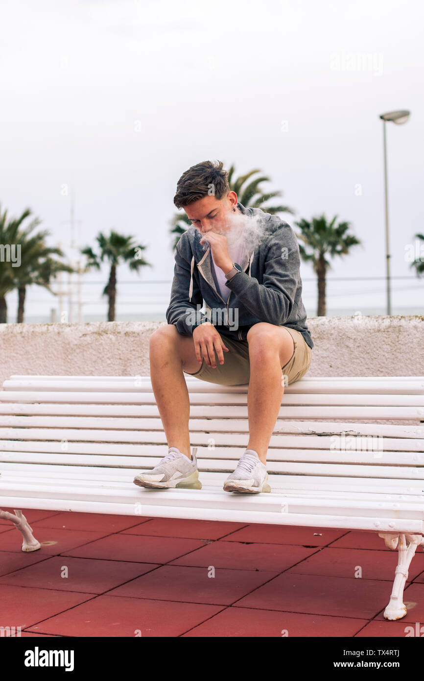 Junger Mann rauchen einen Joint mit Palmen im Hintergrund Stockfoto