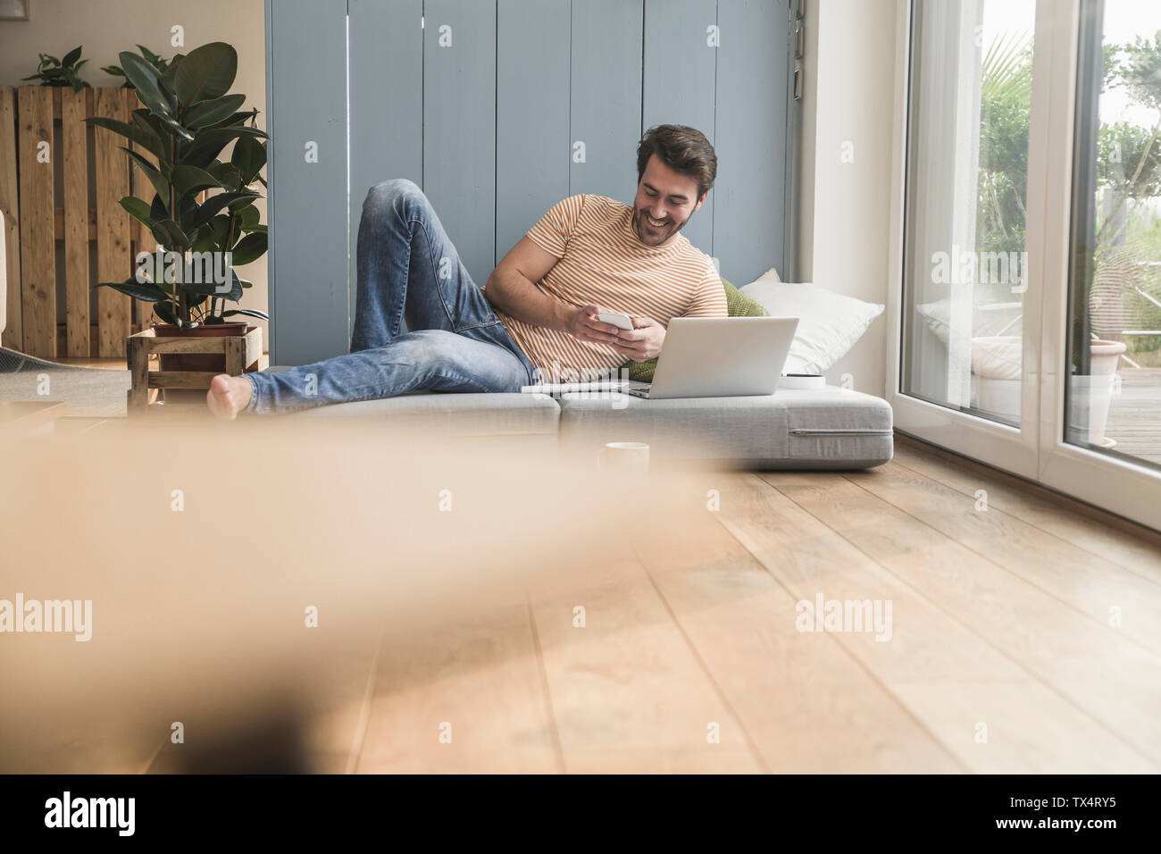 Junger Mann sitzen auf Matratzen, mit Laptop, Notizen Stockfoto
