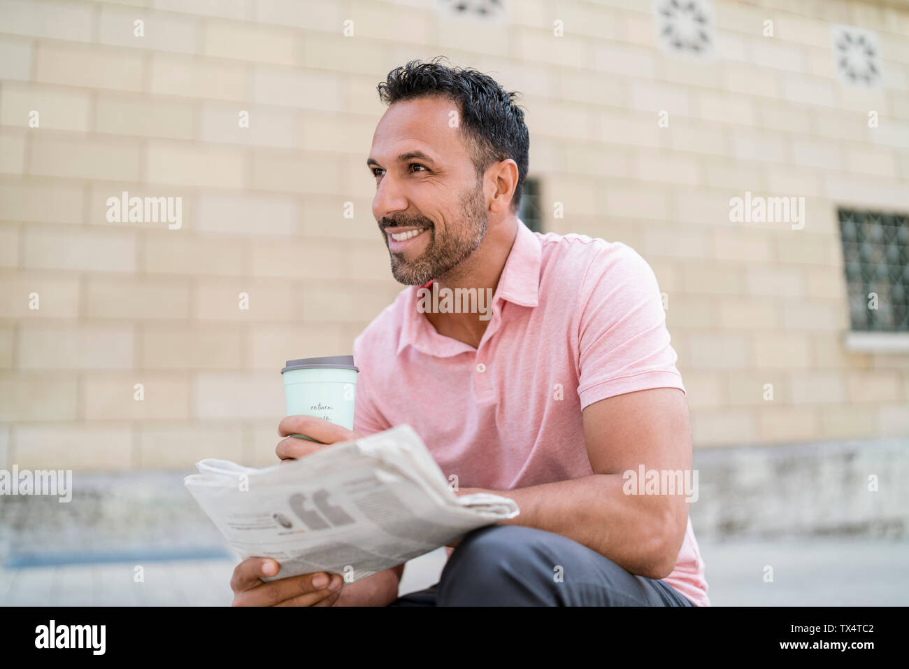 Lächelnder Mann mit Kaffee und Zeitung zum Mitnehmen in der Stadt Stockfoto