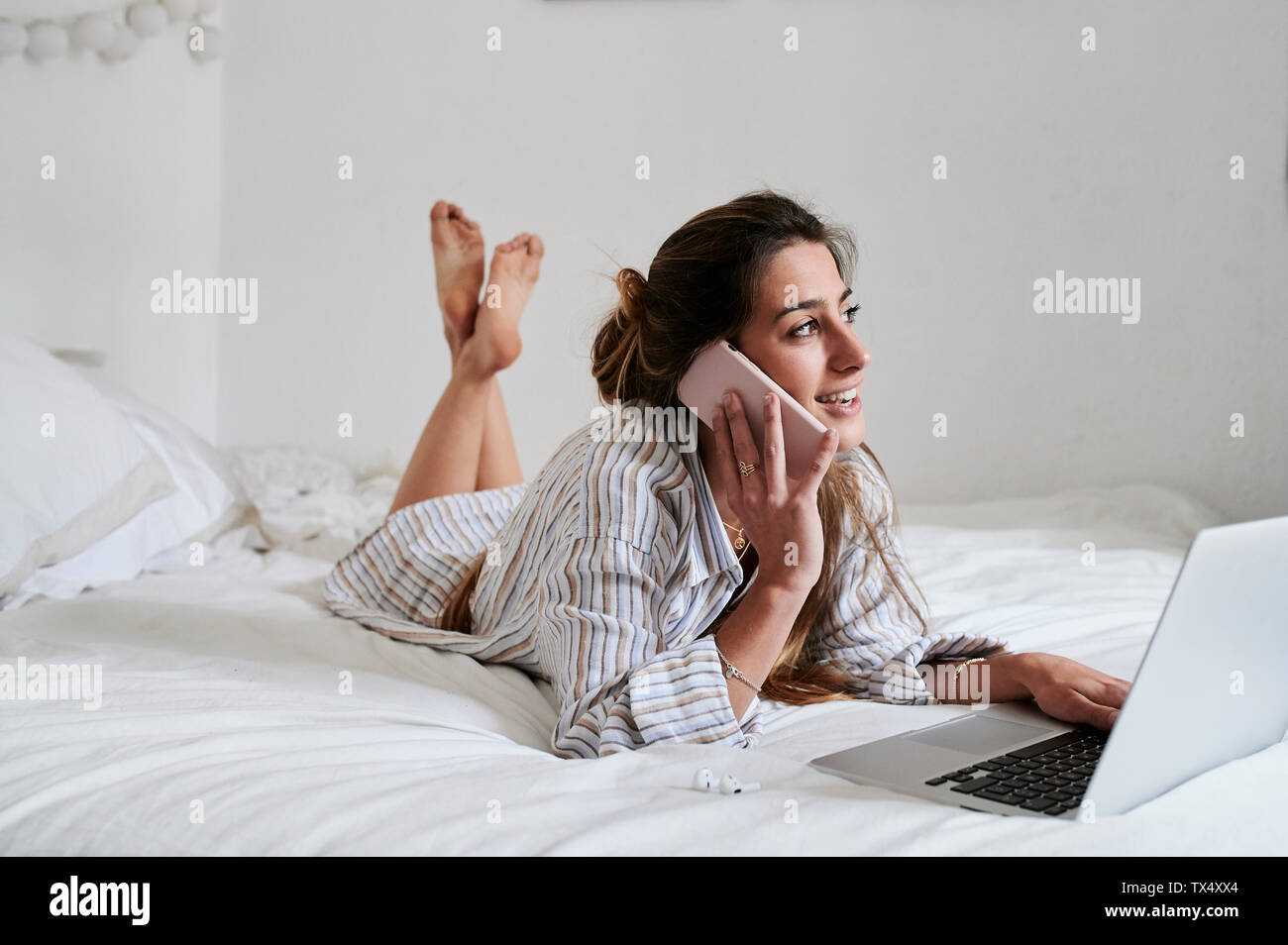 Junge Frau im Bett liegt, mit Laptop, Telefonieren Stockfoto