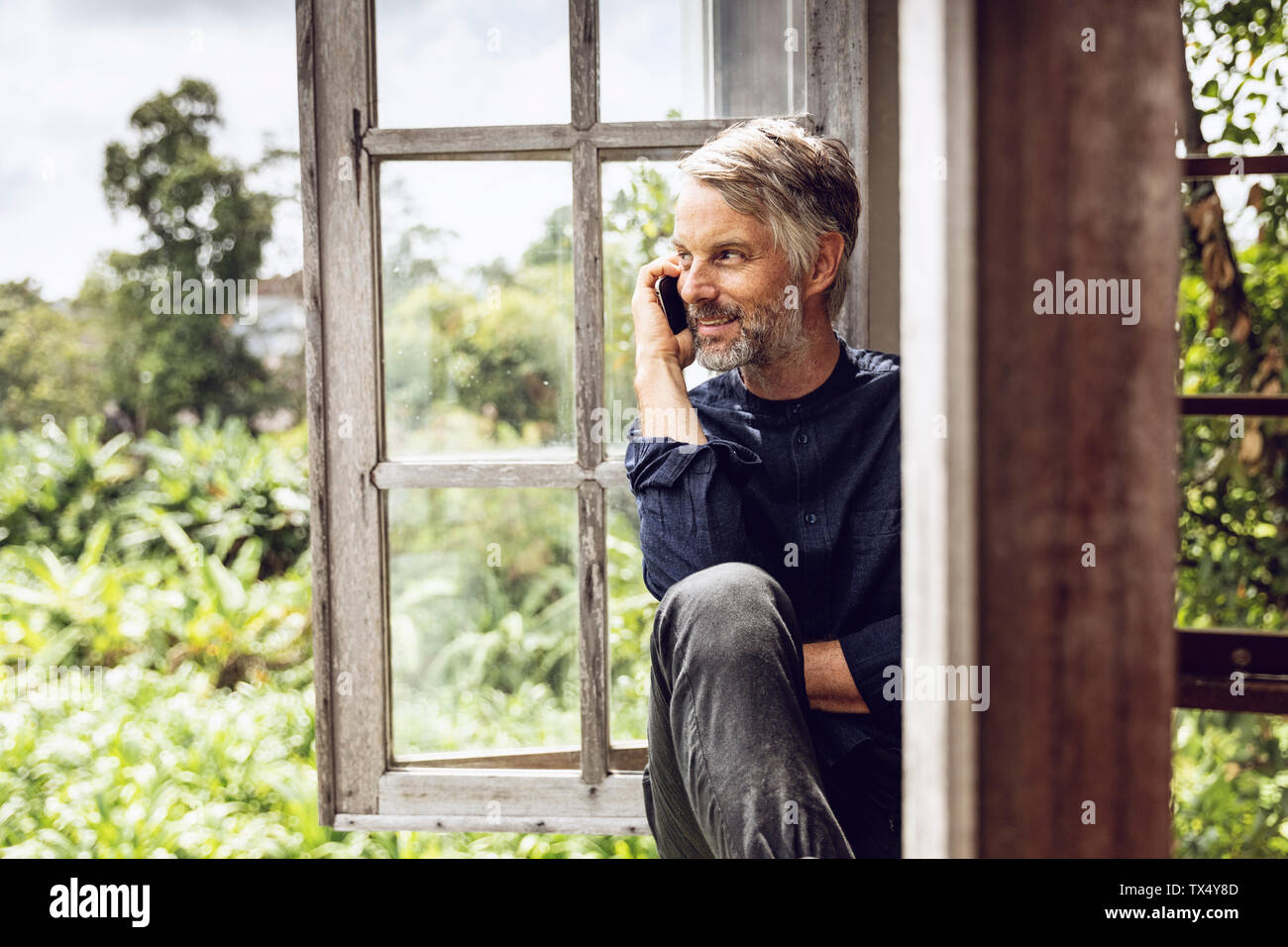 Mann auf Handy sitzen im Fenster in tropischer Umgebung Stockfoto