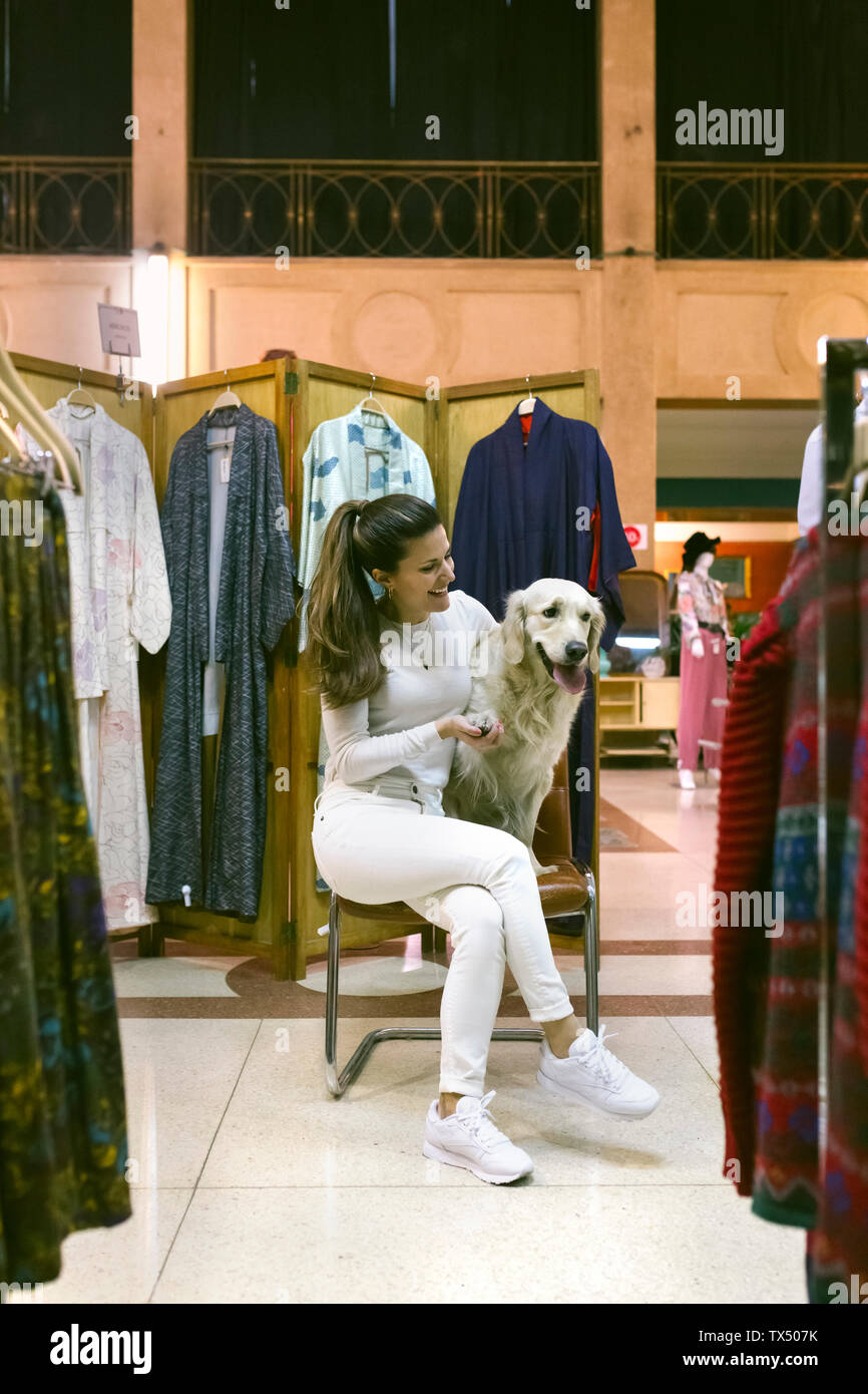 Lächelnde Frau mit Hund sitzen auf Stuhl in einem Vintage Boutique Stockfoto