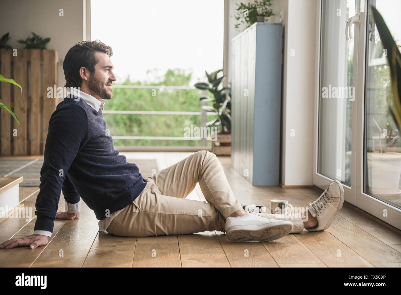 Junger Mann saß auf dem Boden und schaute aus dem Fenster, entspannend Stockfoto