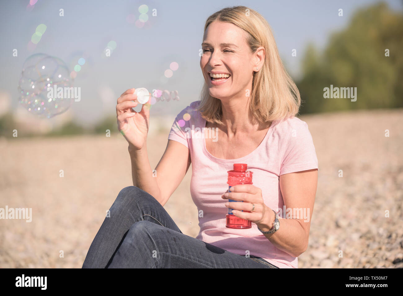 Gerne reife Frau bläst Seifenblasen auf Pebble Beach Stockfoto