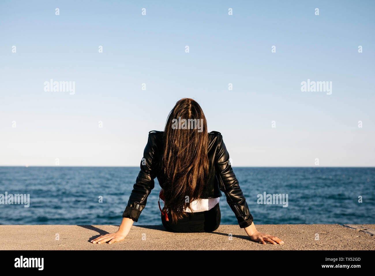 Junge Frau sitzt auf einer Wand, Meer im Hintergrund Stockfoto